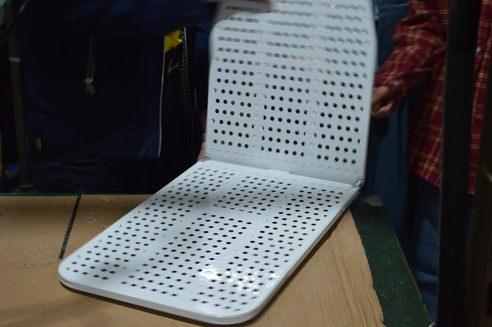 Paneles perforados de una tabla de planchar unidos por bisagras y parcialmente abiertos sobre un banco de montaje